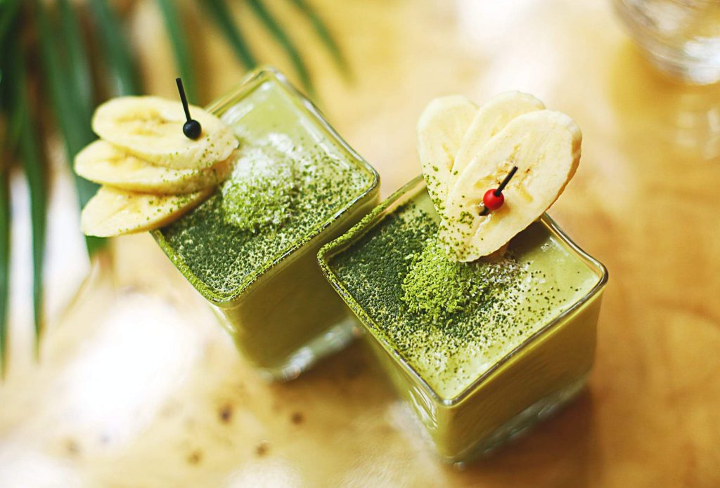 Immune Booster- Kiwi Spinach Banana And Oats Smoothie drink kept in a glass with bananas on the glass sides