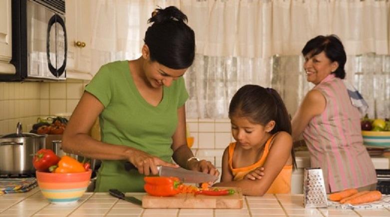 Maintaining health of body and mind, while earning from home! Mother in the kitchen showing her daughter how to cut vegetables while they are happily looked by the their grandmother.