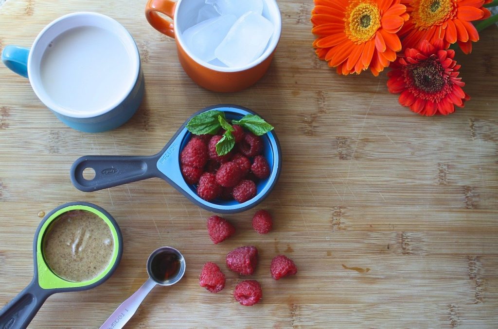 Easy And Healthy Summer Drinks For Kids. On the table are kept a cup of milk, a cup of ice, some strawberries, a tbsp of cocoa, chocolate paste and some flowers