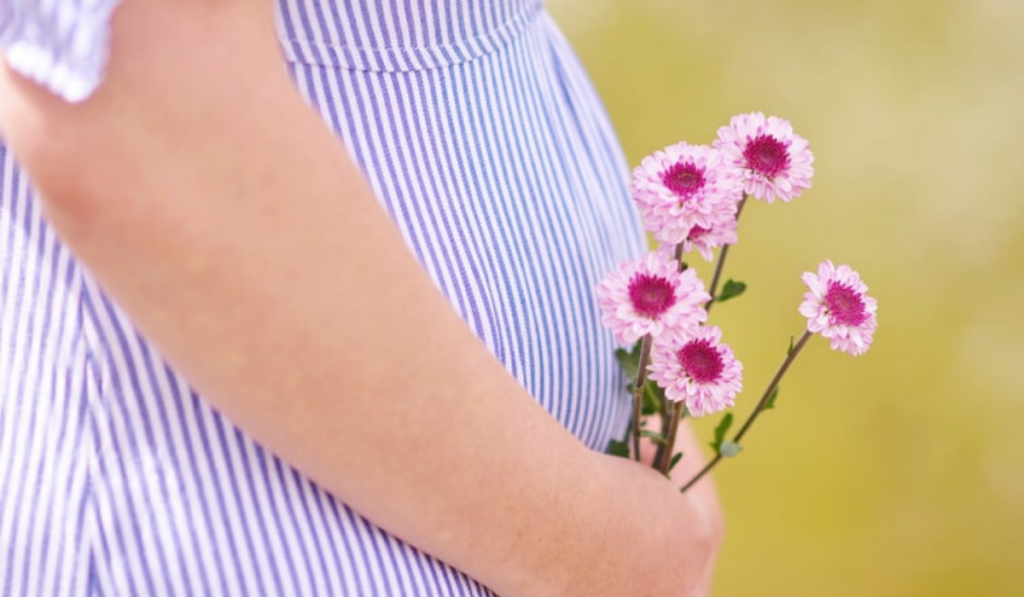 Is Millets An Ideal Food During Pregnancy? A pregnant women standing with flowers in hand.