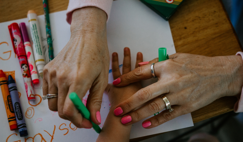 5 Drawing Games For Kids. A mothers hand drawing the hands of her kids with crayons.