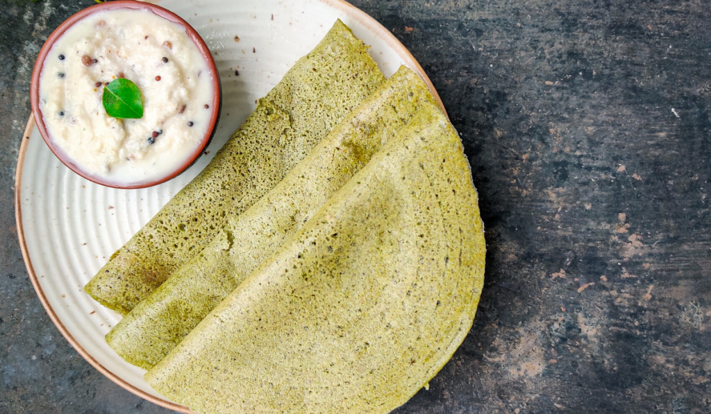 Thin And Crispy Sprouts And Millets Dosa Recipe. Two dosa kept on a white plate with chutney on the side.