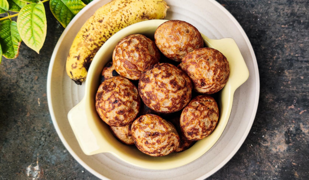 Healthy Breakfast Recipe For Fussy Eaters - Banana Oats Paniyaram kept on a plate along with a banana on it's side.